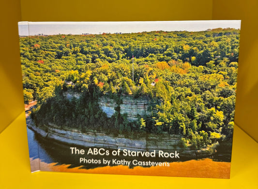 A hardcover book titled 'The ABCs of Starved Rock' by Kathy Casstevens, featuring a cover photograph of a forested cliffside, displayed against a bright yellow background.