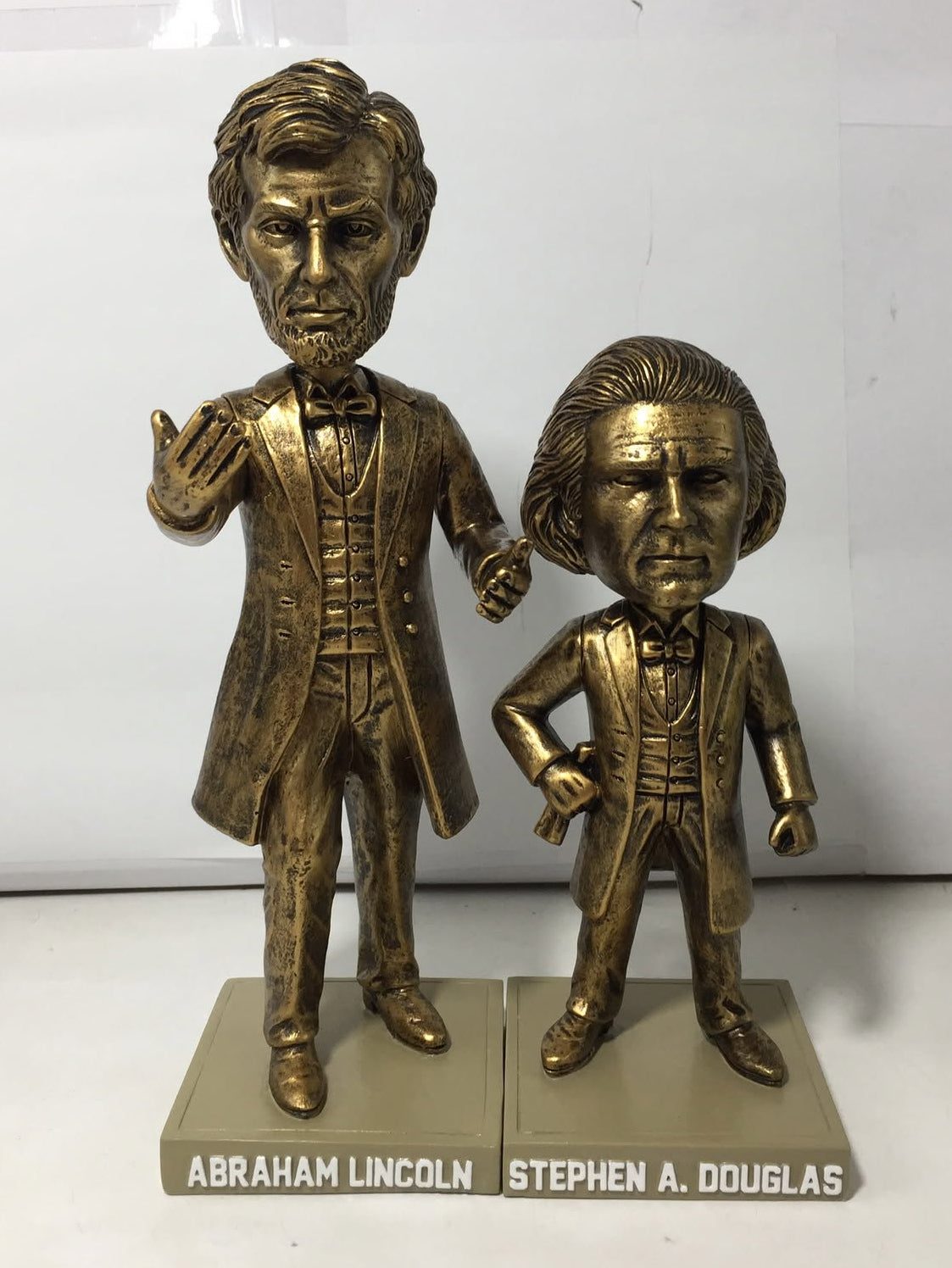 Two bronze-colored bobblehead figurines of Abraham Lincoln and Stephen A. Douglas on matching display bases, photographed against a plain white background.